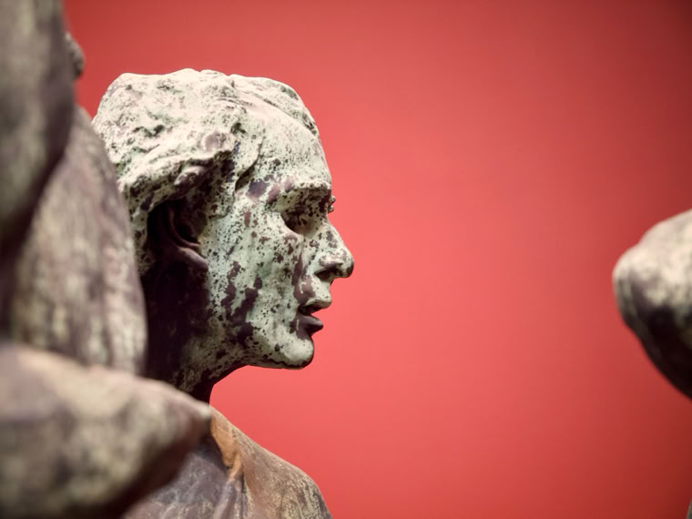 Bronze statue of a person's profile against a red background.