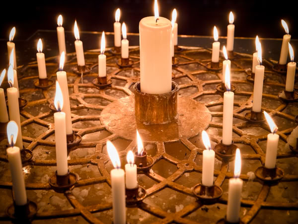 A large candle surrounded by smaller lit candles arranged in a circular pattern on a decorative surface.