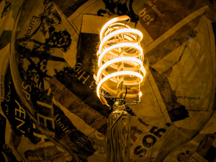 A glowing spiral light bulb against a background of overlapping newspaper pages.